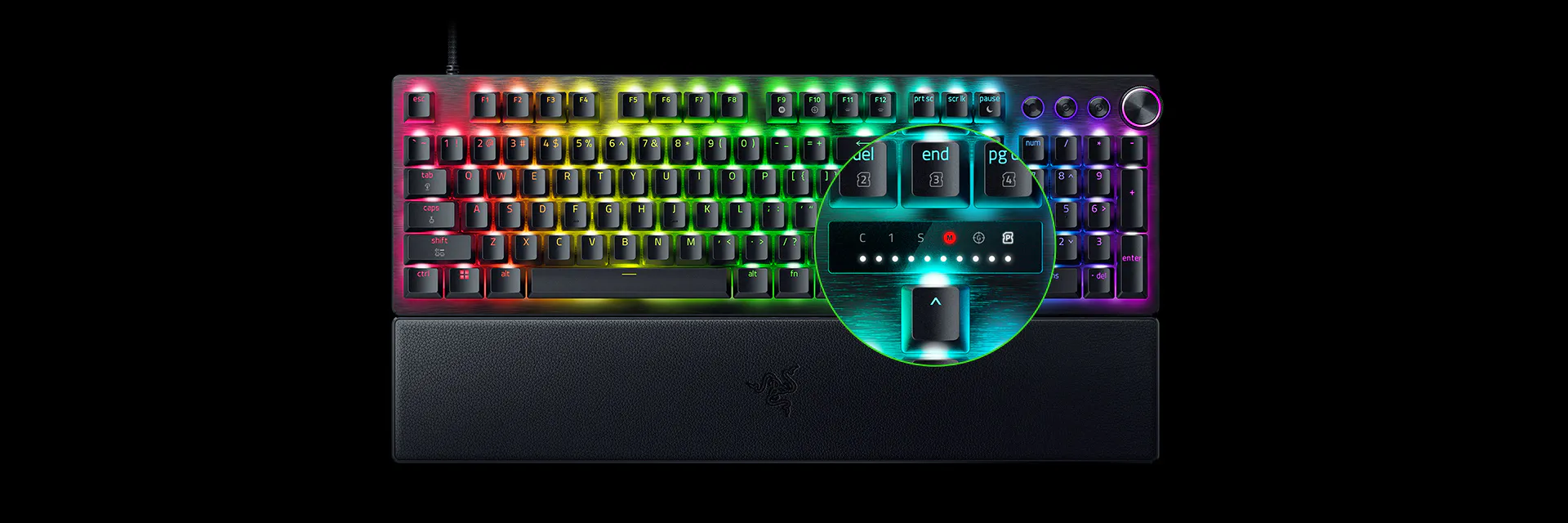 RGB backlit gaming keyboard with a control dial on the top right, a circular magnified inset showing key functions, black background.