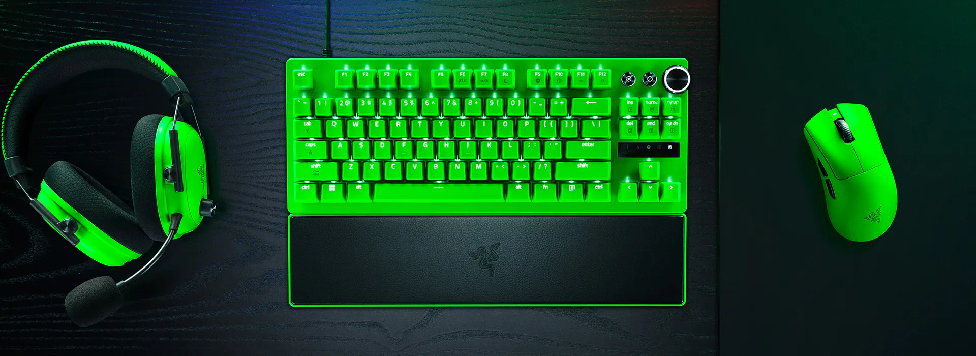 Green-lit gaming headset, keyboard, mouse on a black desk, all glowing bright green.