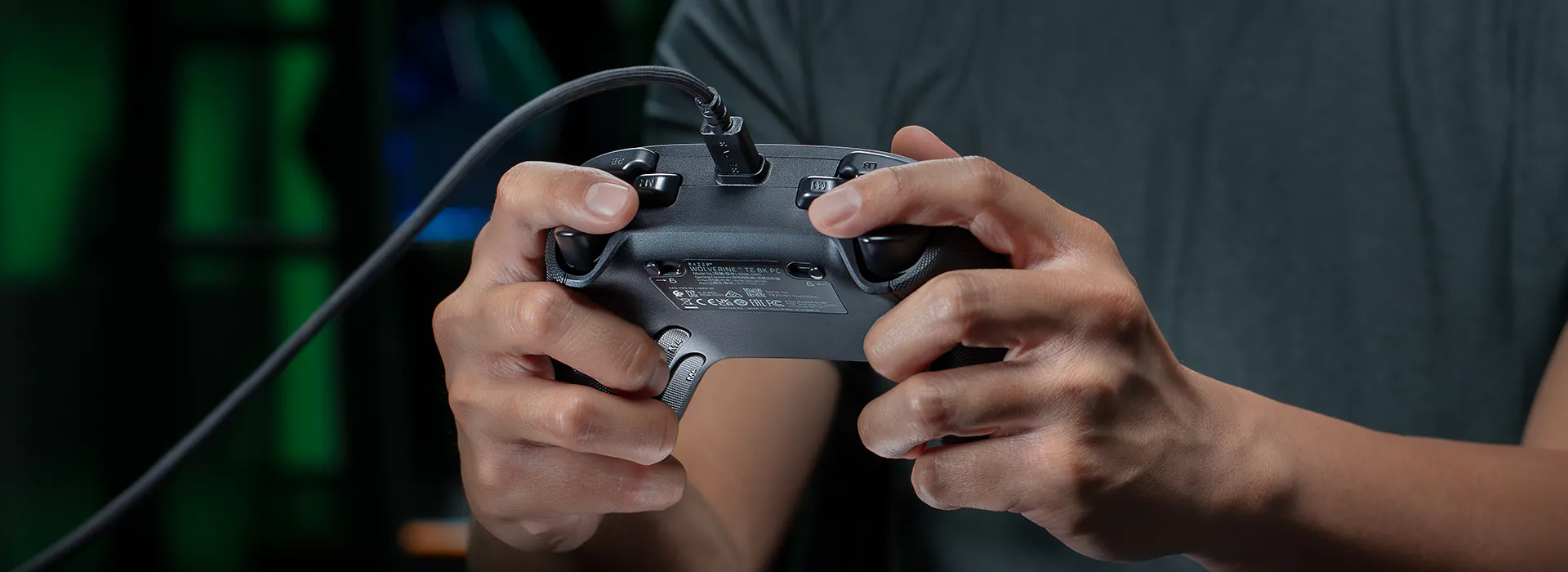 Person holding a game controller, focusing on hands and device, with a dark, blurred background. The controller has visible buttons and a cable.