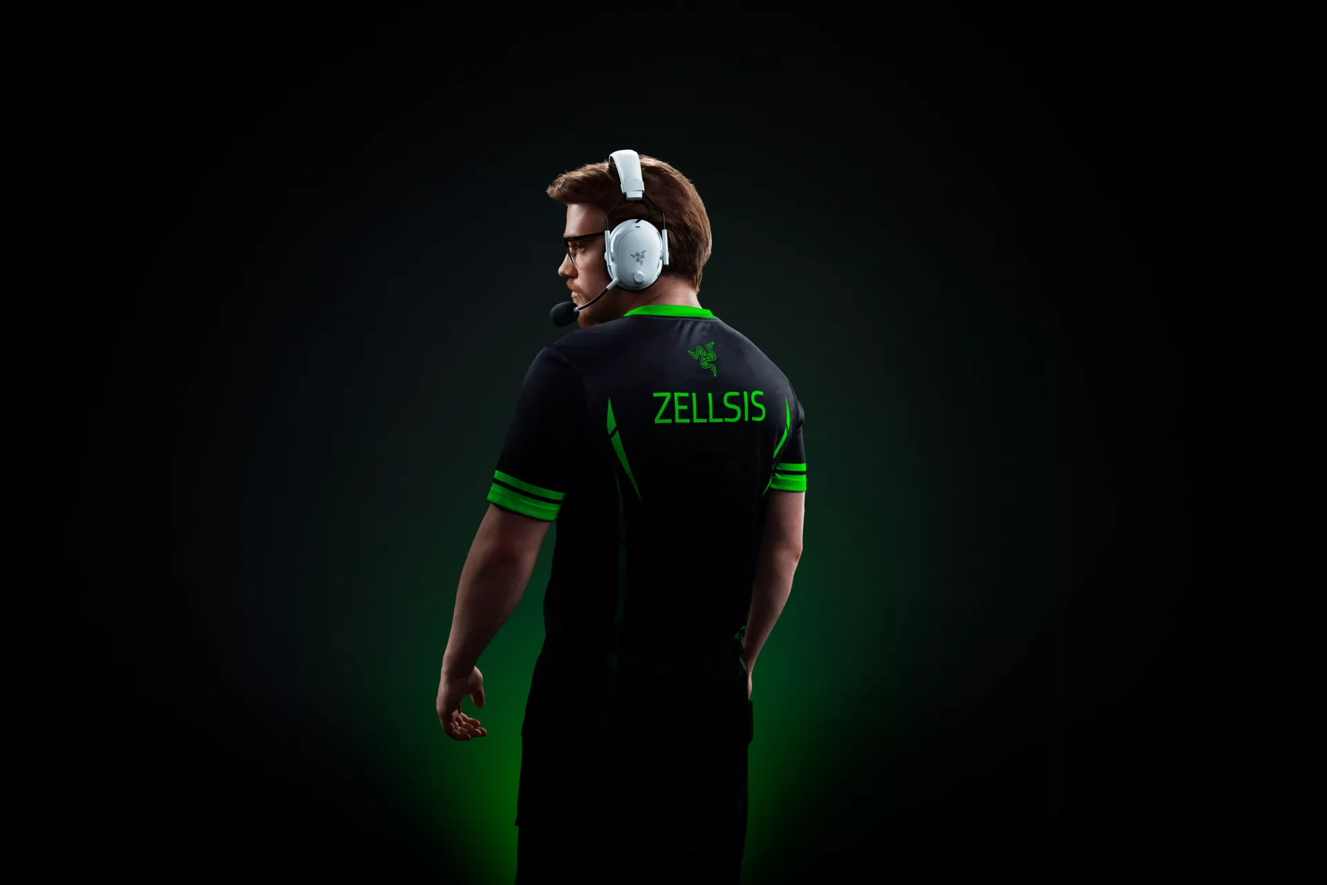 Professional esports player Zellsis wearing a white Razer BlackShark V3 Pro and a Team Razer jersey, standing against a dark background with green lighting accents.