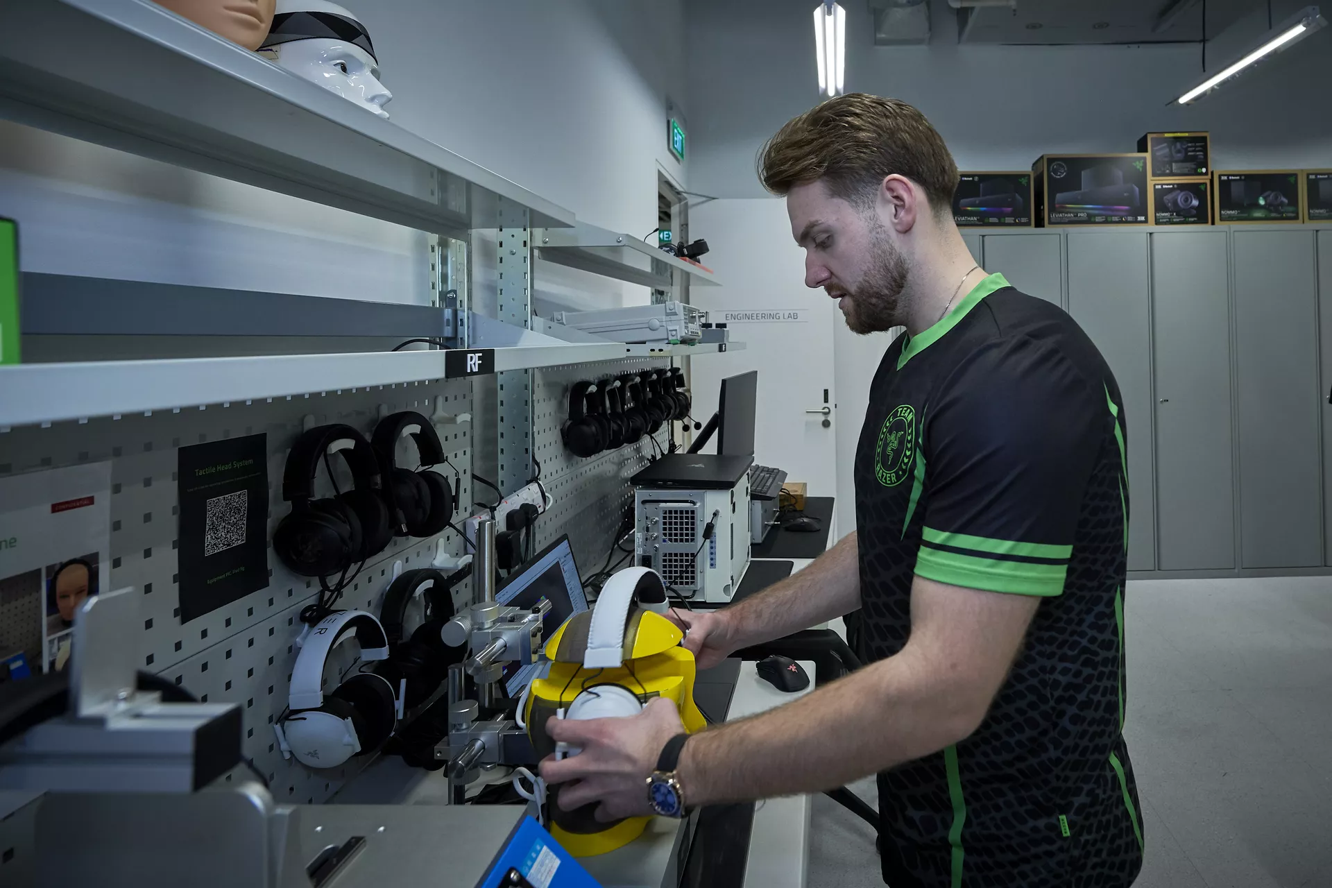 NiKo helping to run durability and fit tests on a white Razer BlackShark V3 Pro in an engineering workspace.