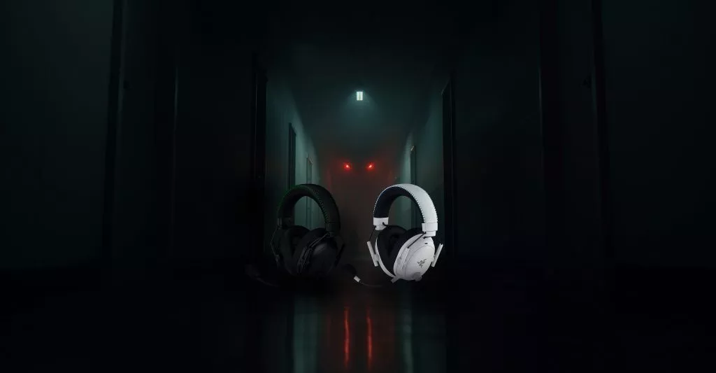 Razer BlackShark V3 Pro gaming headsets in black and white placed in a dark hallway, with glowing red eyes in the background.