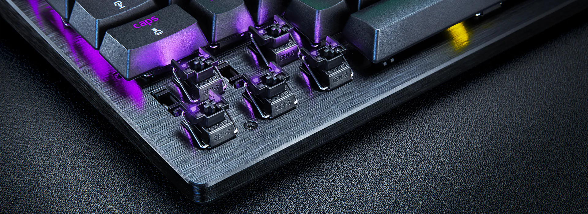 Close-up of a mechanical keyboard with visible switches and keycaps, emitting purple LED lighting over a brushed metal base.