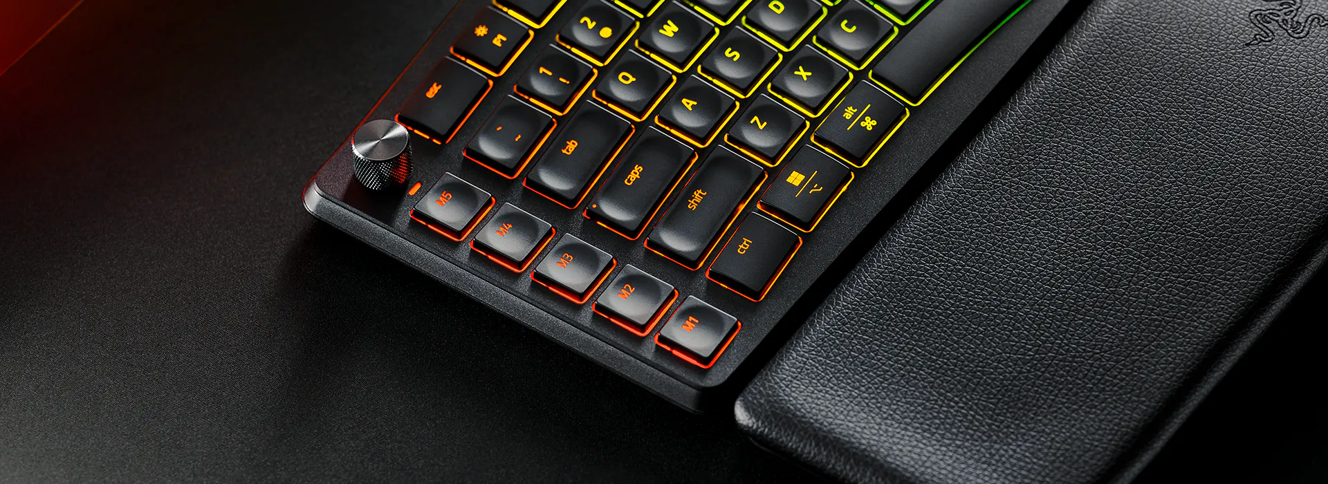 Close-up of a gaming keyboard with illuminated orange-backlit keys, including macro keys labeled M1 to M5, and a textured wrist rest.