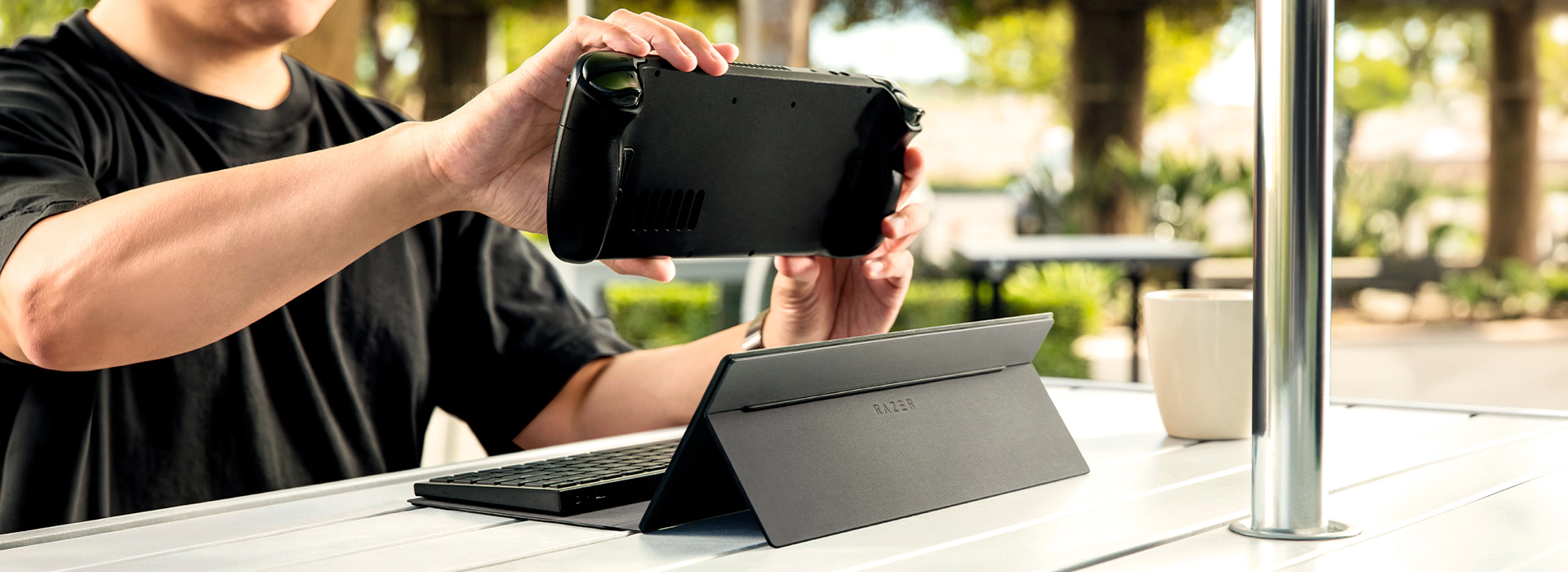 Handheld console positioned above an unfolded case stand embossed with the Razer logo, with keyboard base attached