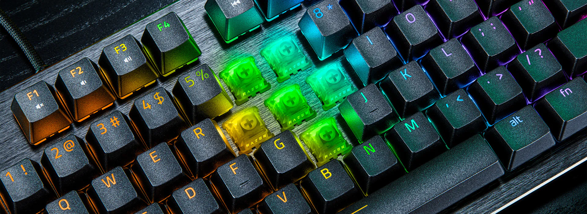 RGB-backlit mechanical keyboard with four removed green and yellow keycaps labeled "RAZER" revealing green switches.