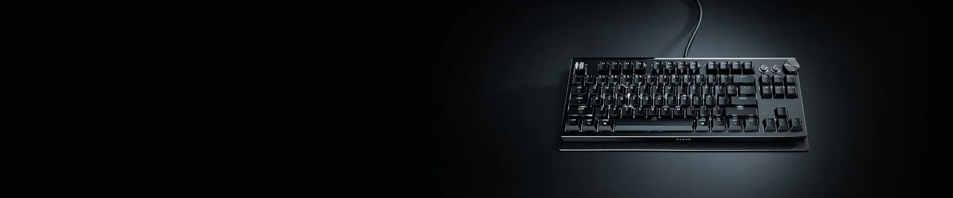 A black mechanical keyboard with a numeric keypad and dial, connected by a wire, on a dark surface.