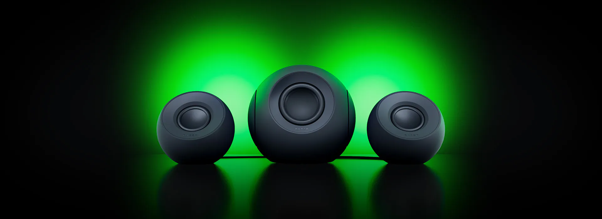 Three black spherical speakers with a central one emitting green light, set against a dark background with a green glow.