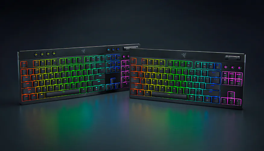 Two Razer RGB backlit mechanical keyboards with rainbow-colored keys on a dark surface, one with a number pad, one without.