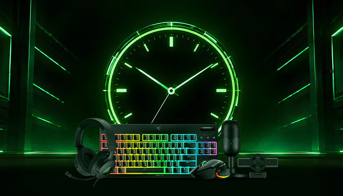A gaming setup with a rainbow-backlit keyboard, gaming mouse, headset, microphone, and controller in front of a large neon green clock display.
