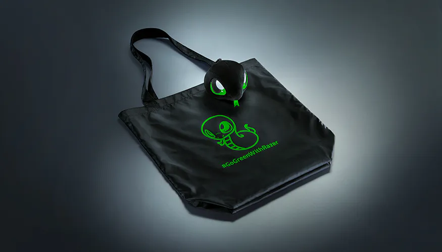 A black tote bag with green graphics of a smiling robot and octopus, and the hashtag "#GreenWithRazer". A black Razer gaming headset rests on it.