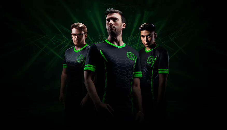 Three esports players pose seriously in black and green jerseys with neon accents, set against a dark, dynamic green-lit background.