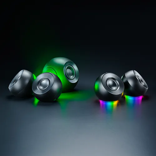 Six small black speaker units with colorful rainbow lights beneath, set on a dark surface, against a black background.