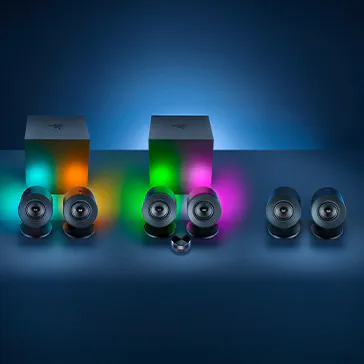 Three speaker sets with colorful glowing lights, two boxes behind, each with a different RGB glow: green, pink, and orange.