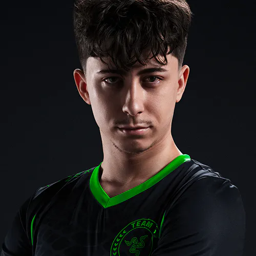 Portrait of a young man with dark curly hair, wearing a black sports jersey with green accents and a "TEAM RAZER" logo, against a dark background.