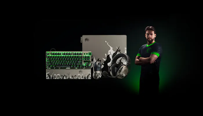 A gamer with arms crossed stands next to gaming gear: a keyboard, mouse, headset, and a large box with a splash design; background is dark.