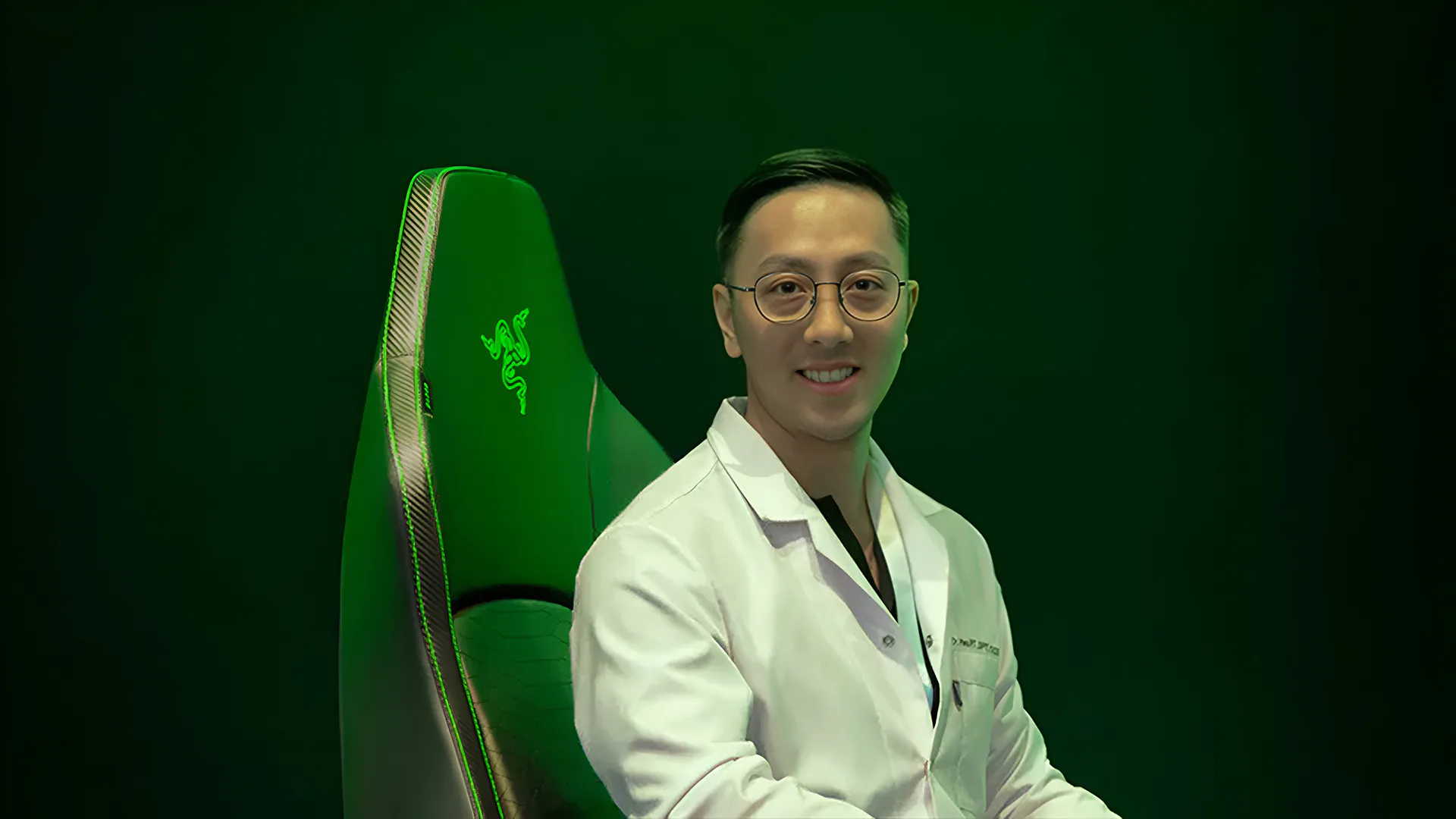 A smiling Doctor Matthew Hsu sits on the Razer Iskur V2.