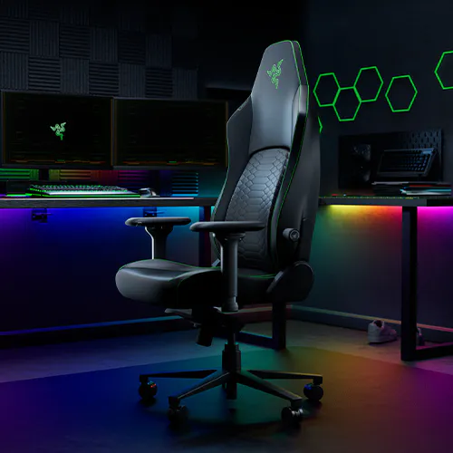 Gaming chair with illuminated RGB background, dual monitors, and hexagon-shaped light pattern on the wall in a dark, tech-themed setup.