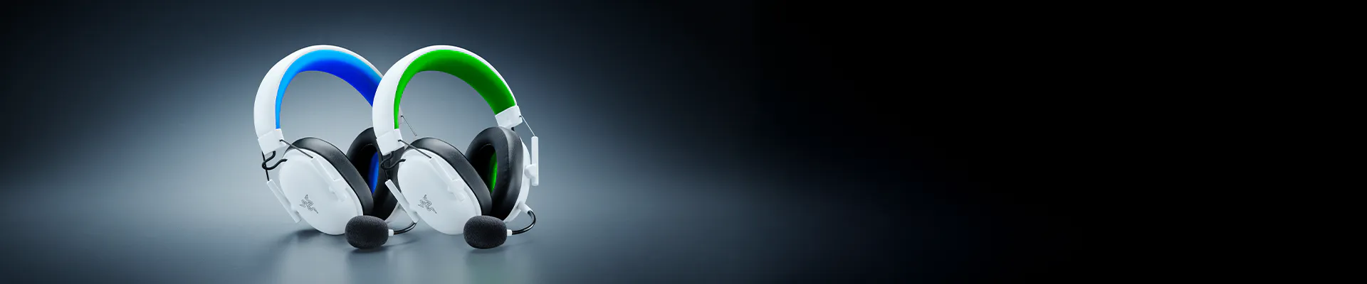 Two gaming headsets with microphones, one with blue accents and one with green, placed on a flat surface against a dark background.