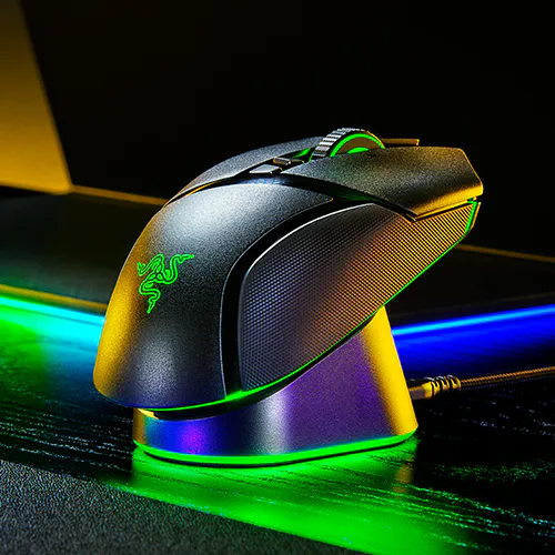 A black gaming mouse with green RGB lighting, placed on a stand with illuminated base, on a textured dark surface.