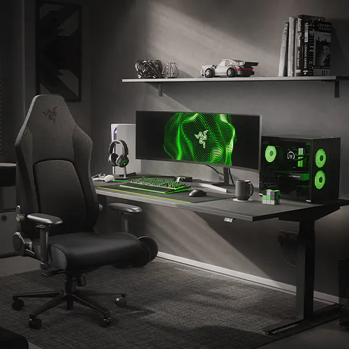 A gaming setup with a black ergonomic chair, triple monitor displaying green graphics, Razer keyboard, mouse, headphones, and a black speaker.