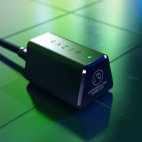 Razer HyperPolling Wireless adapter with a green LED, placed on a tiled surface with green lighting; "RAZER" logo and "HYPERPOLLING WIRELESS" text visible.