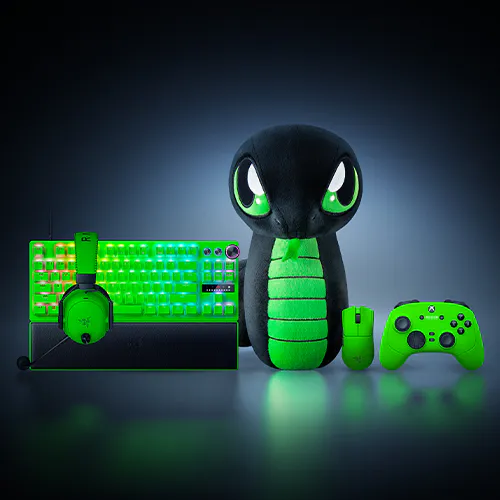 A green gaming setup with a keyboard, headphones, plush snake toy, mouse, and game controller, all illuminated with neon green accents.