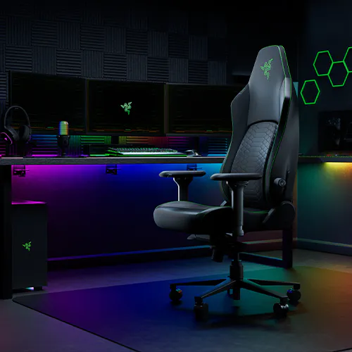 Gaming chair with Razer logo, black leather, ergonomic design, set in a room with glowing RGB lighting, computer setup in the background.