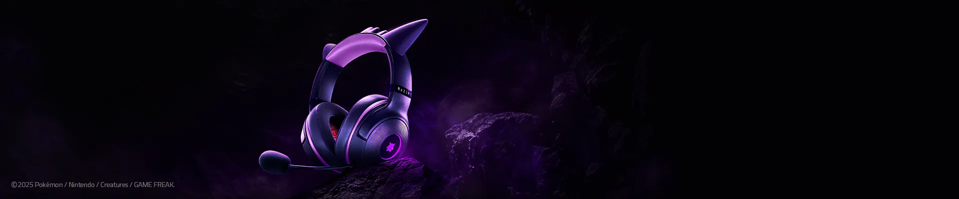 A purple gaming headset with cat-ear speakers, microphone, and Razer logo, set against a dark, rocky background with purple lighting.