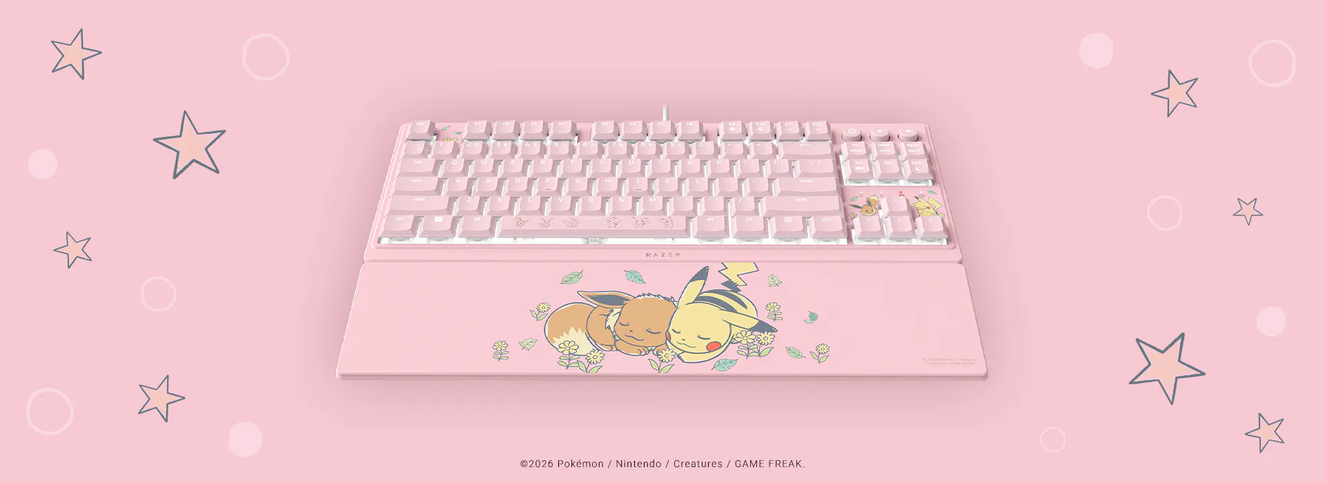 Pink Pokémon-themed keyboard with Pikachu and Eevee characters on the palm rest, surrounded by stars and circles on a pink background.; ©2026 Pokémon / Nintendo / Creatures / GAME FREAK.