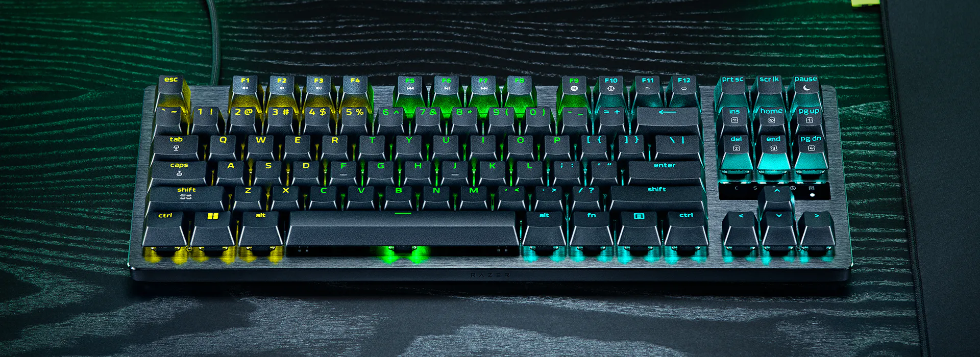 Razer mechanical keyboard with RGB backlighting, black keys with yellow, green, and turquoise accents on a black textured surface.