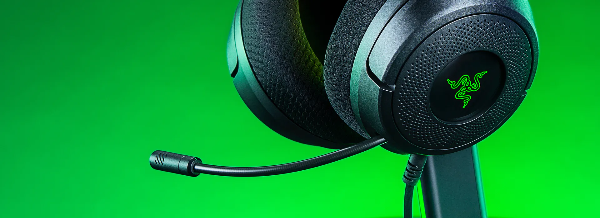 Close-up of Razer gaming headset with mic on black stand against green background, showing the Razer logo on earcup.