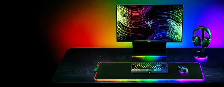 RGB gaming setup with monitor, RGB keyboard, mouse, headset, and a large mousepad on a dark desk with colorful backlighting.