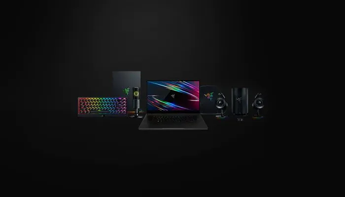 A black background with gaming gear: Razer keyboard, Razer laptop, Razer external drive, Razer speakers, and colorful RGB lighting.