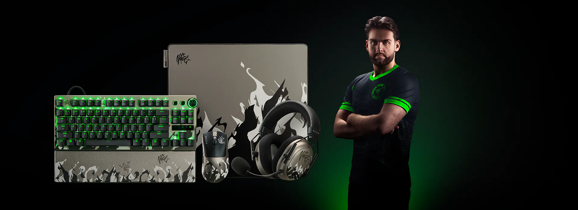 Niko standing with arms crossed next to gaming accessories: keyboard, mouse, headphones, and a laptop.