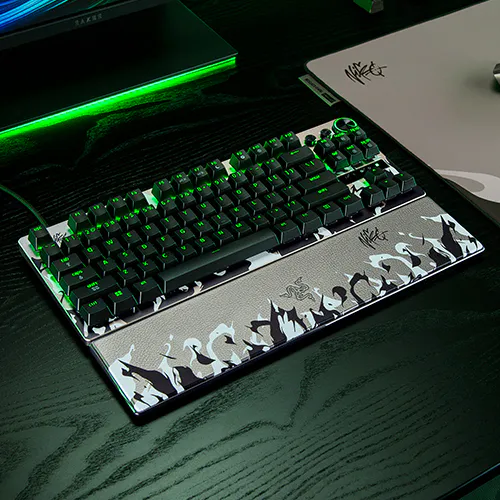 Gaming keyboard with black keys, green backlighting, and a graphic design of dark silhouettes with cats on a silver base.