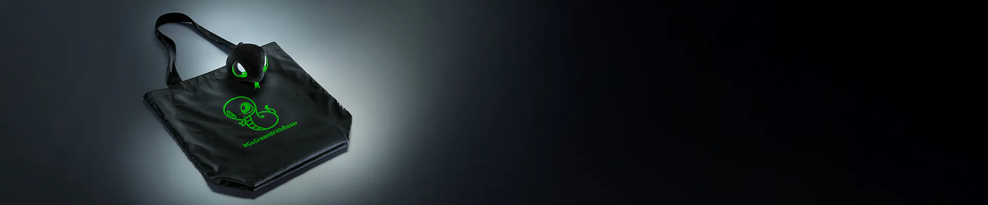 Black tote bag with green Razer logo and hashtag #GoGreenWithRazer; attached black and green earbuds and earbud case with Razer logo.