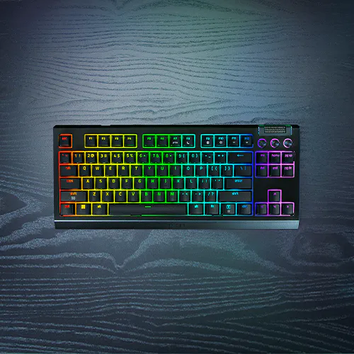 A black RGB mechanical keyboard with rainbow-colored backlit keys on a dark textured surface.