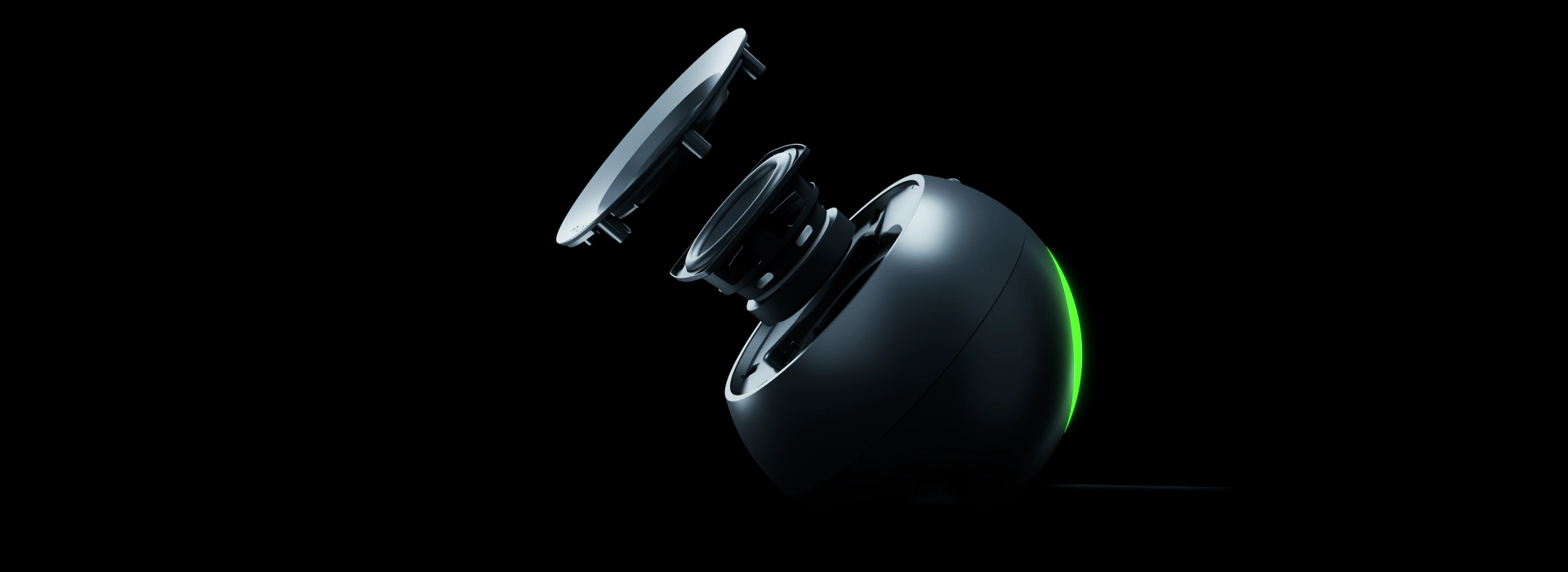 A black, spherical speaker with two disassembled parts floating above, illuminated by a green light on the side, against a black background.