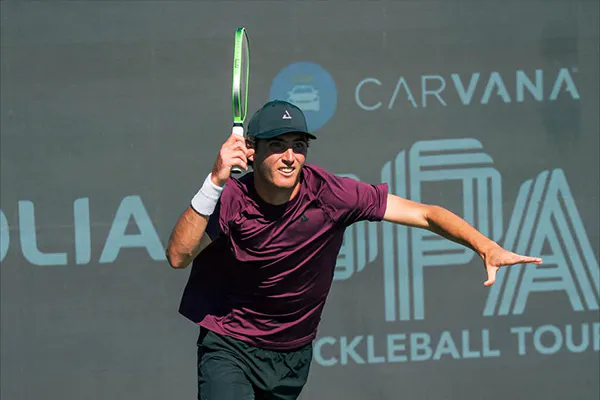 a player celebrates on a pickleball court with a paddle in hand, wearing a black cap, maroon shirt, and black shorts.