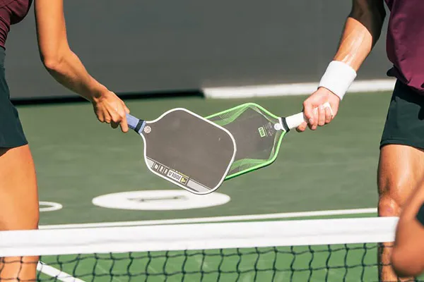 two players tap their paddles after a pickleball match on a court. the paddles are branded.