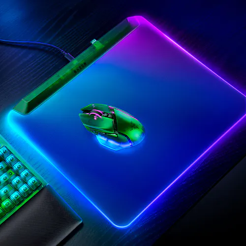 A neon-lit gaming setup with a glowing mouse, Razer-branded pen, backlit keyboard, and illuminated mouse pad with purple, blue, 绿色, and pink lighting.