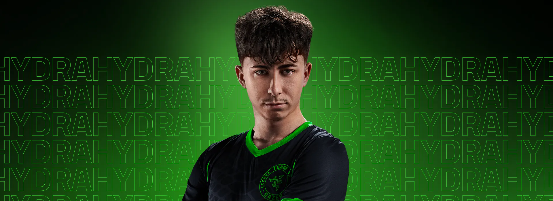 A young man with curly dark hair wearing a black jersey with green accents and a Razer Team logo, posing confidently against a black background.